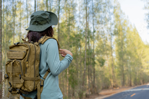 Young Asian girl with a backpack and hat hiking in the mountains during the summer season, a traveler walking in the forest. Travel, adventure, and journey concept. © maya1313