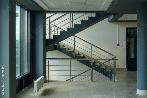 Stairs in a concrete office building in neutral tones, covered with ceramic tiles, with shiny metal railings