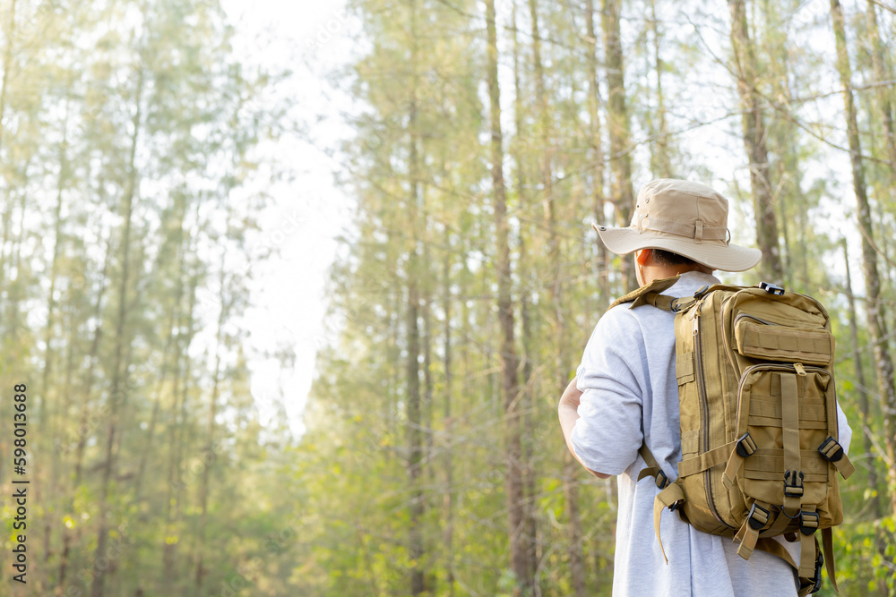 Young Asian man with a backpack and hat hiking in the mountains during the summer season, a traveler walking in the forest. Travel, adventure, and journey concept. Young Asian man with a backpack and hat hiking in the mountains during the summer season, a traveler walking in the forest. Travel, adventure, and journey concept.