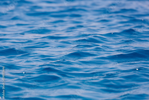 Defocused blurred the motion of blue water surface at the sea  lake. Water surface texture. Abstract beautiful ripples  splashes and bubbles. Banner background. Water waves in sunlight with copy space