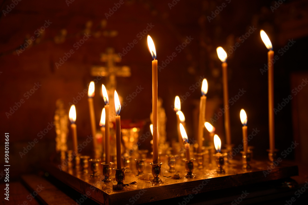 Candles burning on candelabrum in a church, a cross on a background, red tone Candles burning on candelabrum in a church, a cross on a background, red tone