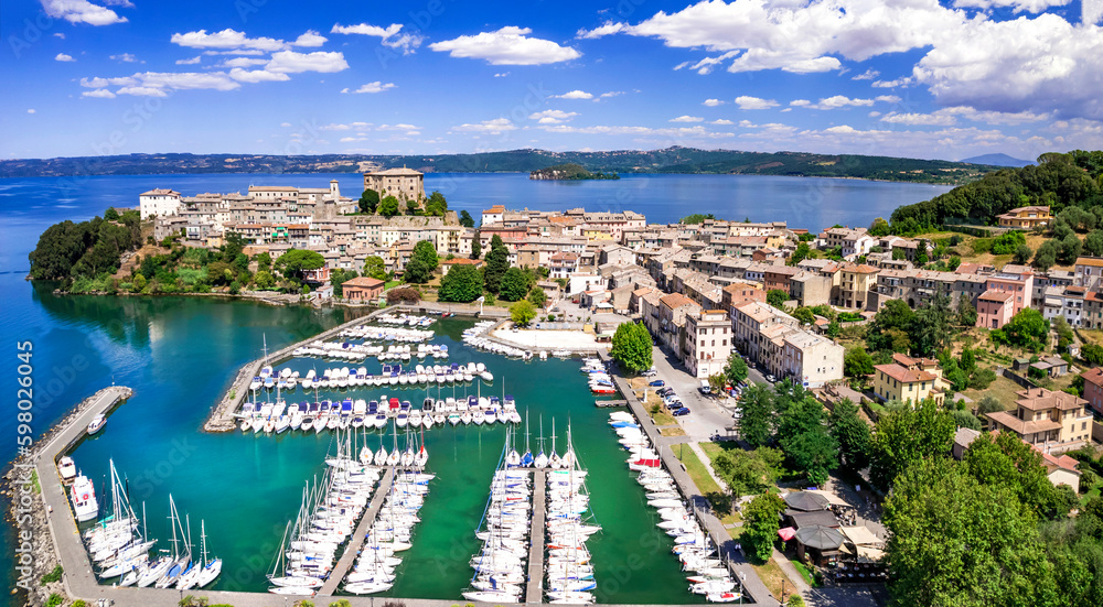 Fototapeta premium Bolsena Lake Italy 6k aerial panorama of Capodimonte medieval village on peninsula. Scenic drone view of luxury yacht marina and ancient castle in Viterbo province. Beautiful Lazio travel destination