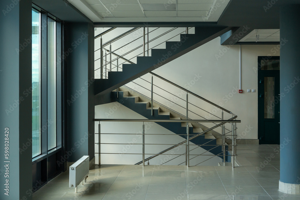 Fototapeta premium Stairs in a concrete office building in neutral tones, covered with ceramic tiles, with shiny metal railings
