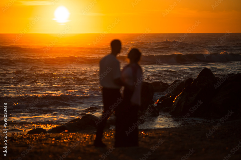 Blurry silhouettes of a couple in love on the ocean during a golden sunset. Blurry silhouettes of a couple in love on the ocean during a golden sunset.