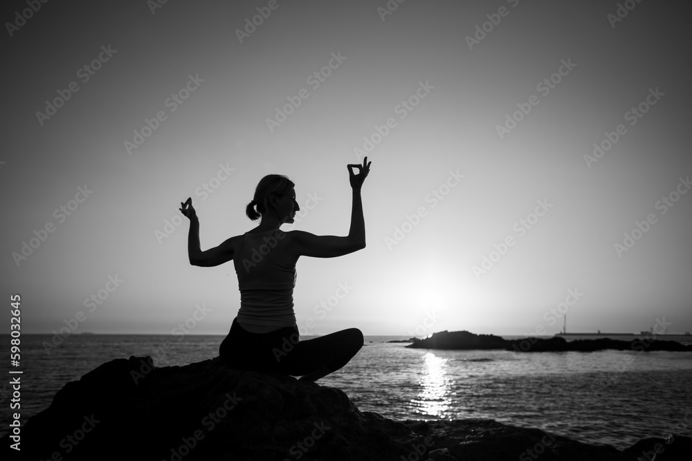 Yoga silhouette female lotus pose on the ocean during a lovely sunset. Black and white photo.