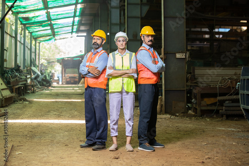 Team of happy confident indian engineers wearing safety hard hat and vest standing at industrial factory, male and female professional workers looking at camera, skill india.
