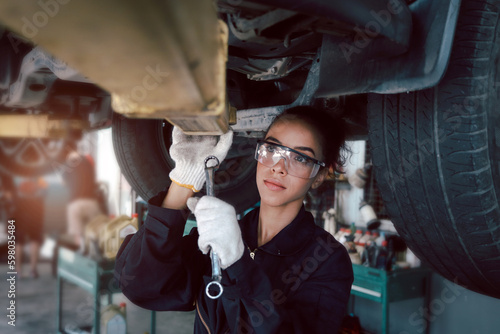 Beautiful female auto mechanic checking wheel tires in garage, car service technician woman repairing customer car at automobile service, inspecting vehicle underbody and suspension engine system.