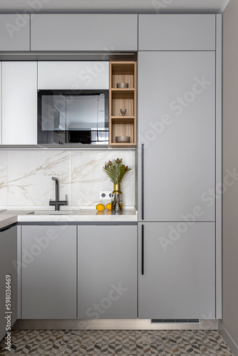 kitchen with a marble wall, white and gray facades, a sink, a microwave, decorated with a vase of flowers and tangerines