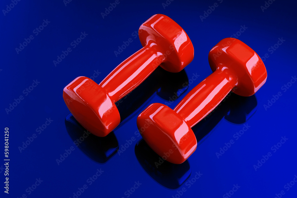 A pair of red dumbbells is reflected in a blue glass surface. View from above. A pair of red dumbbells is reflected in a blue glass surface. View from above.