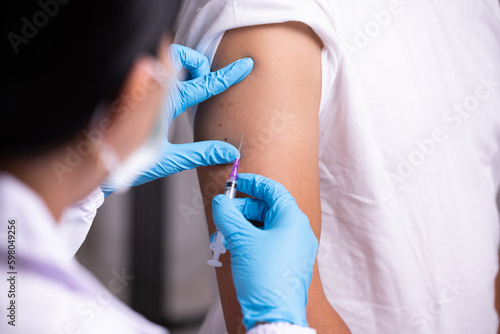 Doctor hand in blue gloves holding influenza vaccine for prevention human.Nurse holding syringe make injection in shoulder of patient in hospital.Covid-19 or coronavirus vaccine. photo
