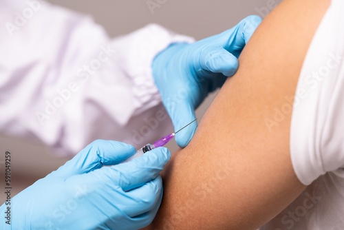 Doctor hand in blue gloves holding influenza vaccine for prevention human.Nurse holding syringe make injection in shoulder of patient in hospital.Covid-19 or coronavirus vaccine. photo