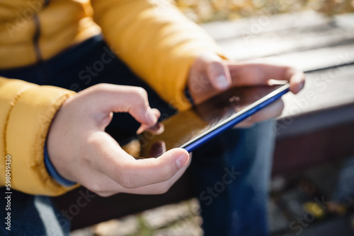 Close up of hands. candid portrait of caucasian teen boy in yellow jacket using smartphone outdoors. communication on the go. Playing games. Gaming