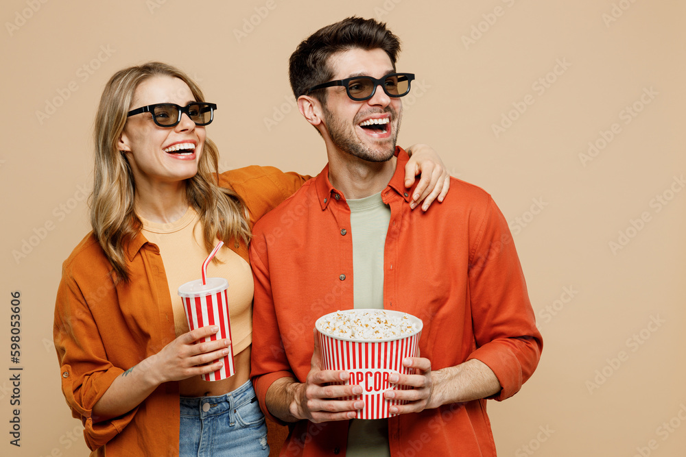 Φωτογραφία Young fun couple two friends family man woman in 3d glasses wear casual clothes watch movie film hold bucket of popcorn cup of soda pop in cinema look aside isolated on plain beige background studio