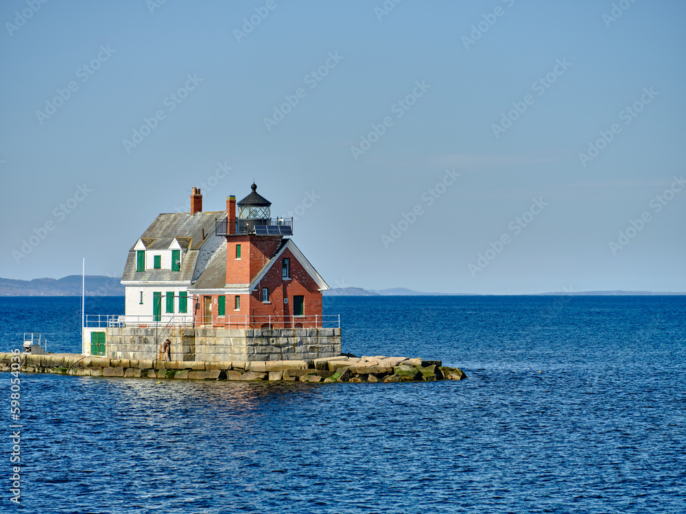 The Rockland Breakwater Lighthouse as seen from the ferry heading back into Rockland harbor with the town of Rockland maine in the background
