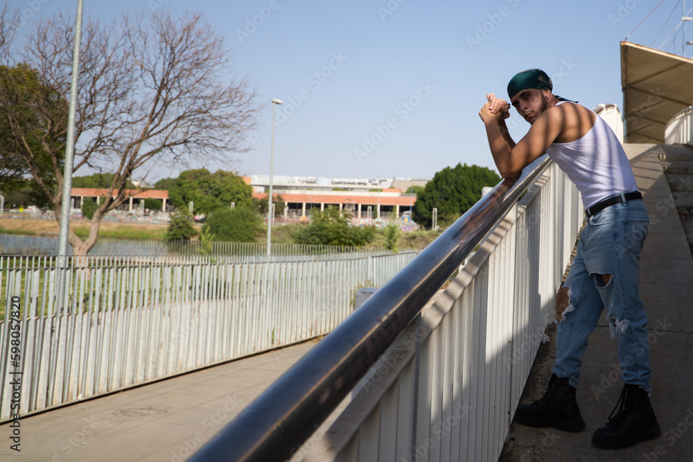 Portrait of a young handsome man dressed in jeans and white t-shirt and green headscarf. The young man is leaning on railing. Street fashion and modern youth culture.