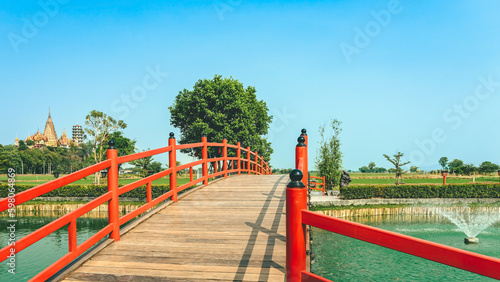 Beautiful view of Japanese style red wooden bridge over emerald pond with fountains against nature of paddy field outdoors. Japanese style garden with unique red wooden bridge. Beautiful landscape.