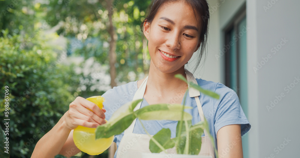 Close-up cheerful happy Asian girl wear apron hold pot on her hand watering plants at cozy home garden. Gently water a plants by using water spray, Gardening making homework domestic life concept. Close-up cheerful happy Asian girl wear apron hold pot on her hand watering plants at cozy home garden. Gently water a plants by using water spray, Gardening making homework domestic life concept.
