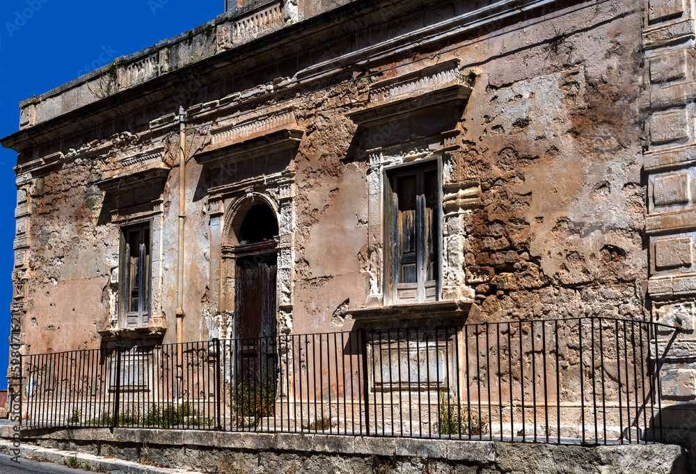 old abandoned and decaying one-storey house with a door and two windows, built in the typical Sicilian style, against an intensely blue sky