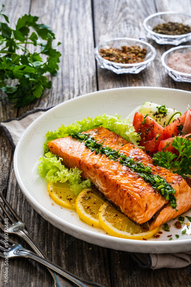 Seared salmon steak with fried potatoes and fresh vegetable salad served on wooden table
Seared salmon steak with fried potatoes and fresh vegetable salad served on wooden table