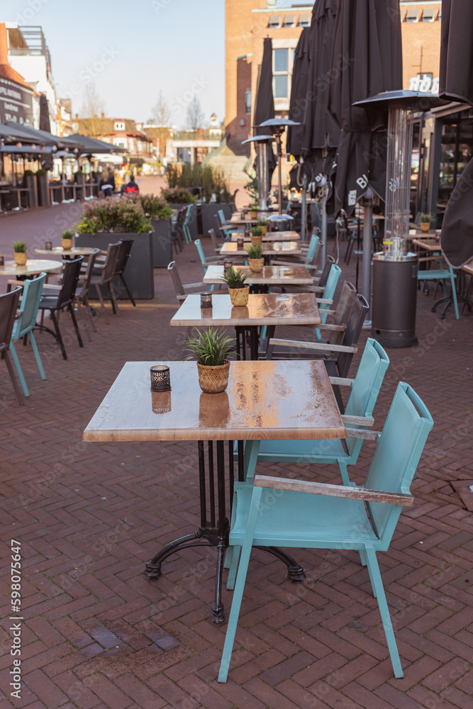Naklejka premium Outdoor seating area of a restaurant with teal chairs and wooden tables, still empty on a sunny day