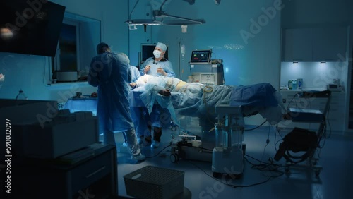 Long shot of plastic surgery procedure, patient lying under anaesthetic on operating table. Medical staff operates in dark illuminated operating room. High quality 4k footage Generative AI