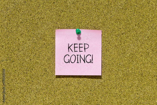 Keep going text on pink post-it paper pinned on bulletin cork board. This message can be used in business concept about keep going.