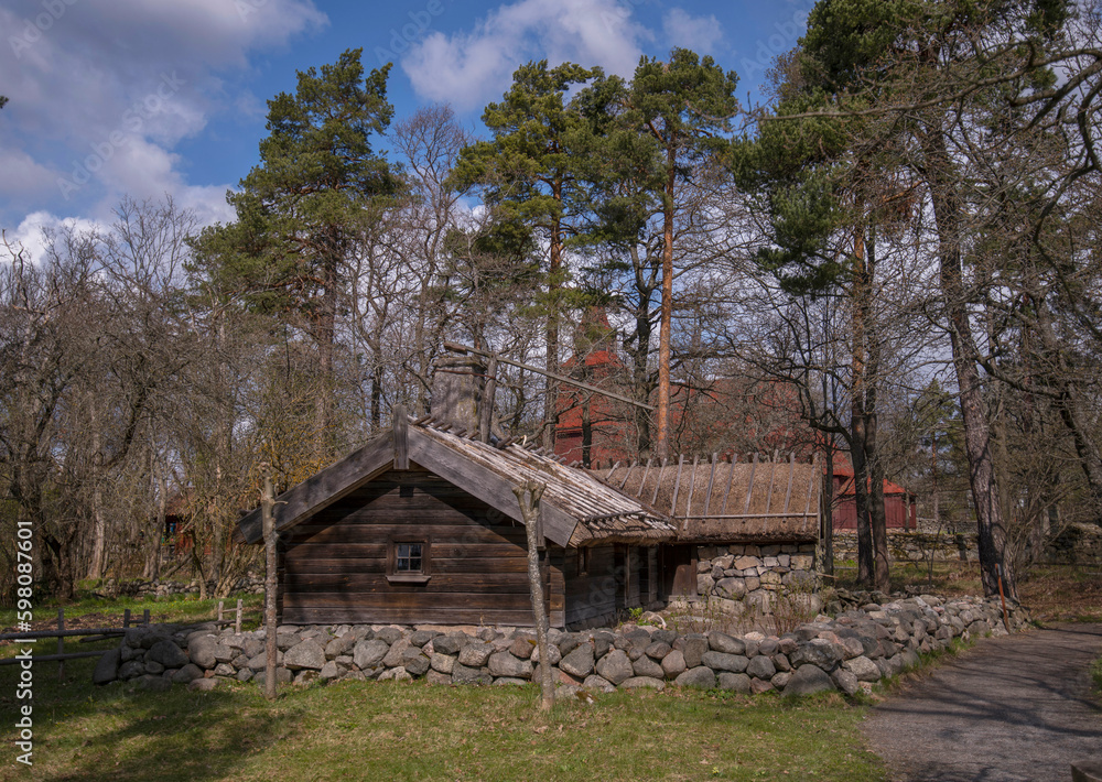 Old 1700s wood log house, turf roof and chimney with lock, Hornborgarstugan, rebuilt in a park, a sunny spring day in Stockholm