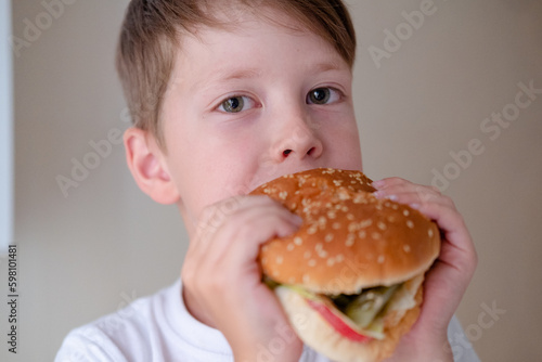 close-up portrait of a little boy eating a huge burger  on a white background