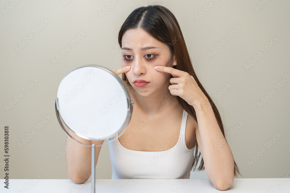 Bored, insomnia asian young woman, girl looking at mirror hand touching under eyes with problem of black circles or panda puffy, swollen and wrinkled on face. Sleepless, sleepy healthcare person. Bored, insomnia asian young woman, girl looking at mirror hand touching under eyes with problem of black circles or panda puffy, swollen and wrinkled on face. Sleepless, sleepy healthcare person.