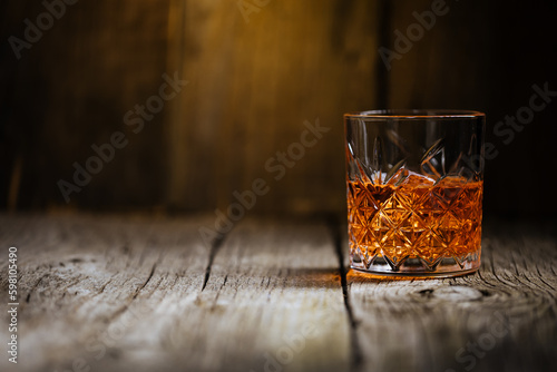Foto A glass of Whiskey on a rustic wooden board, that can be surface of barrel
