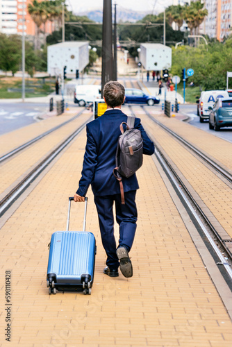 Stylish businessman in a suit with a suitcase is walking along the tracks from the train © Alfonso Soler