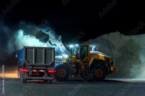 Heavy construction and mining machinery loading a dump truck with gravel in a quarry on the night shift.