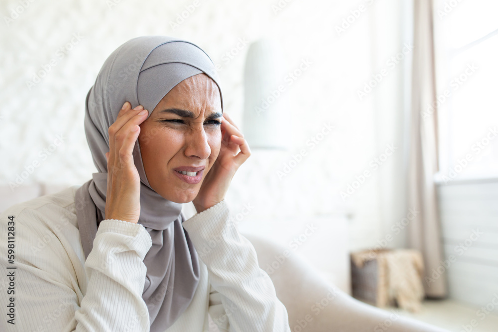 Close-up photo. Depressed and tired state. Portrait of a young woman in a hijab holds her head with her hands, feels severe pain, gives herself a massage, grimaced from tension. Close-up photo. Depressed and tired state. Portrait of a young woman in a hijab holds her head with her hands, feels severe pain, gives herself a massage, grimaced from tension.