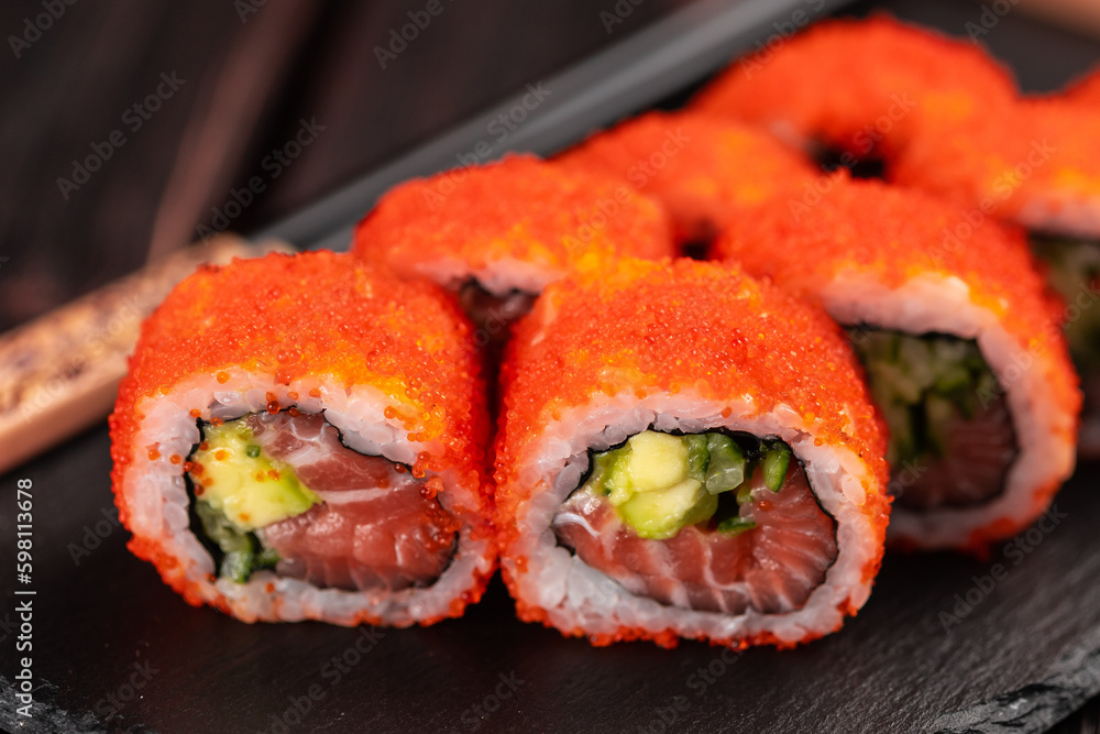 Close up California sushi roll with salmon avocado, cucumber and tobiko caviar served on black board close-up - Japanese food Close up California sushi roll with salmon avocado, cucumber and tobiko caviar served on black board close-up - Japanese food