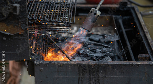 Man lighting up a grill with a gas fire blower torch