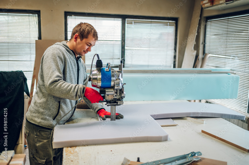Profile view of a worker using a foam cutter at his furniture workshop.