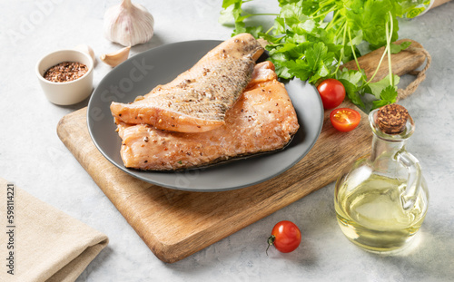 Raw salmon, greased with marinade with spices on a plate on a light background with fresh herbs and vegetables.