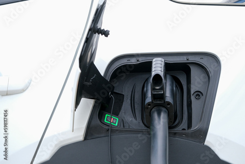 Close up charging white electric car. Electric car charging cable in jack close-up with open cover with instruction sign. Eco friendly car with electric. Seelctive focus. 