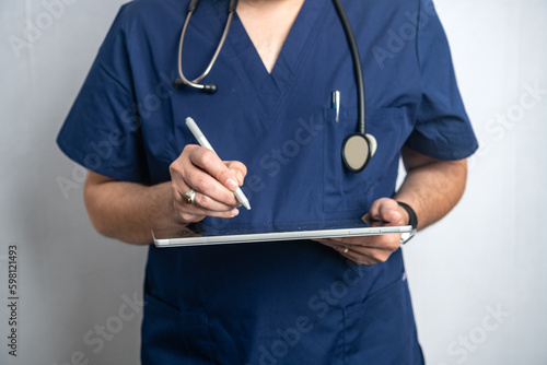 doctor in a blue coat with a stethoscope enters a prescription into a tablet computer.