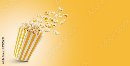 Popcorn flying out of yellow white striped paper box isolated on yellow background with copy space. Splash, levitation of popcorn grains. © katyamaximenko