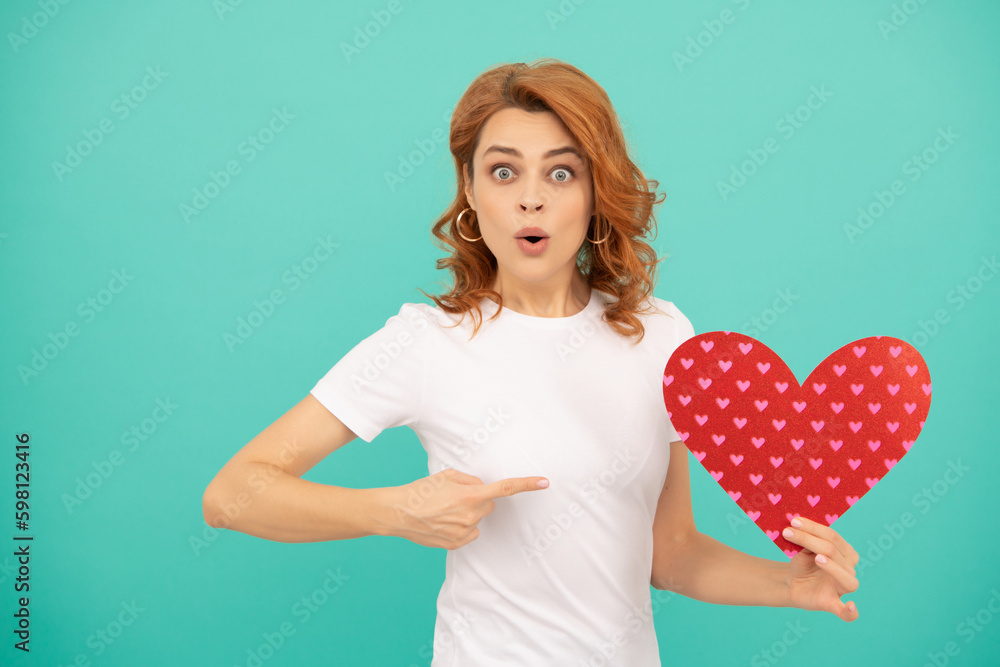 surprised young woman with red heart on blue background. point finger surprised young woman with red heart on blue background. point finger