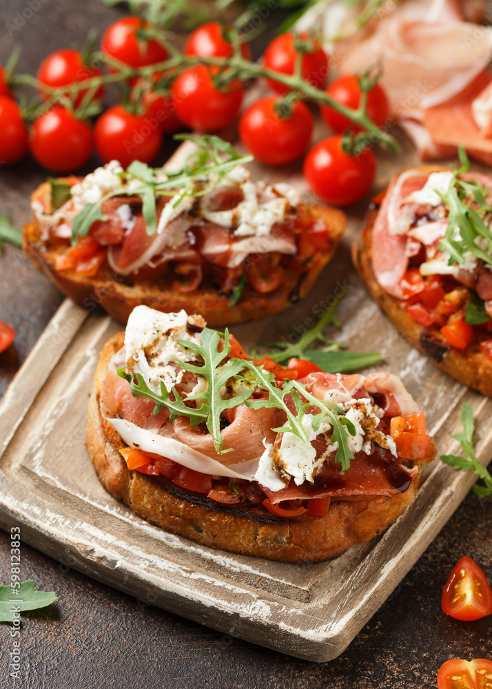 Parma ham and tomato bruschetta served on wooden board with mozzarella, wild rocket leaves and balsamic vinegar
