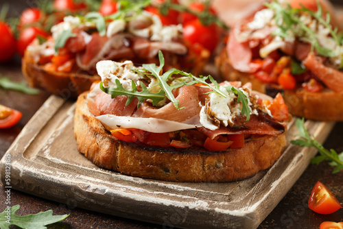 Parma ham and tomato bruschetta served on wooden board with mozzarella, wild rocket leaves and balsamic vinegar