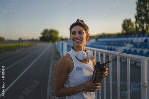 One woman stand at stadium with supplement water bottle take a brake