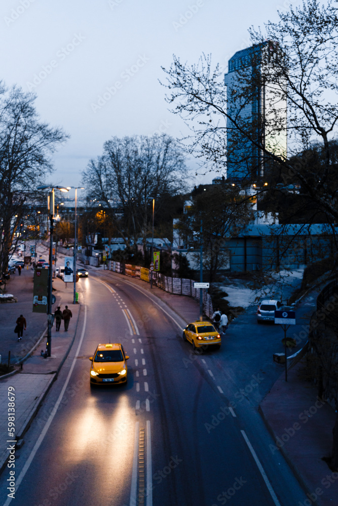 Obraz premium Urban living street. The movement of taxi drivers, pedestrians, the evening metropolis, city with many billboards, lanterns. Central street, outskirts of the town. Futurism concept