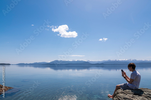 Tableau sur toile Adolescente disfrutando de una video llamada por celular desde la costa del Lago Nahuel Huapi en la ciudad de Bariloche, Patagonia, Argentina