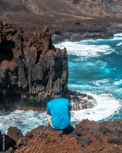 A young man sitting on the volcanic trail in the village of Tamaduste on the coast of the island of El Hierro, Canary Islands, Spain. vertical photo photo