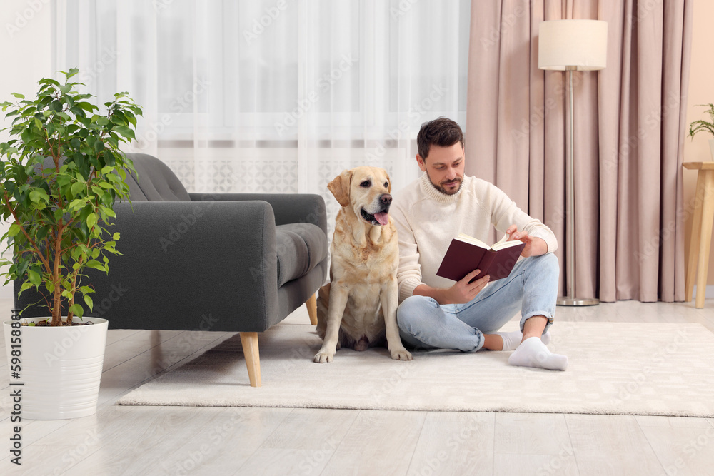 Man reading book on floor near his cute Labrador Retriever at home Man reading book on floor near his cute Labrador Retriever at home