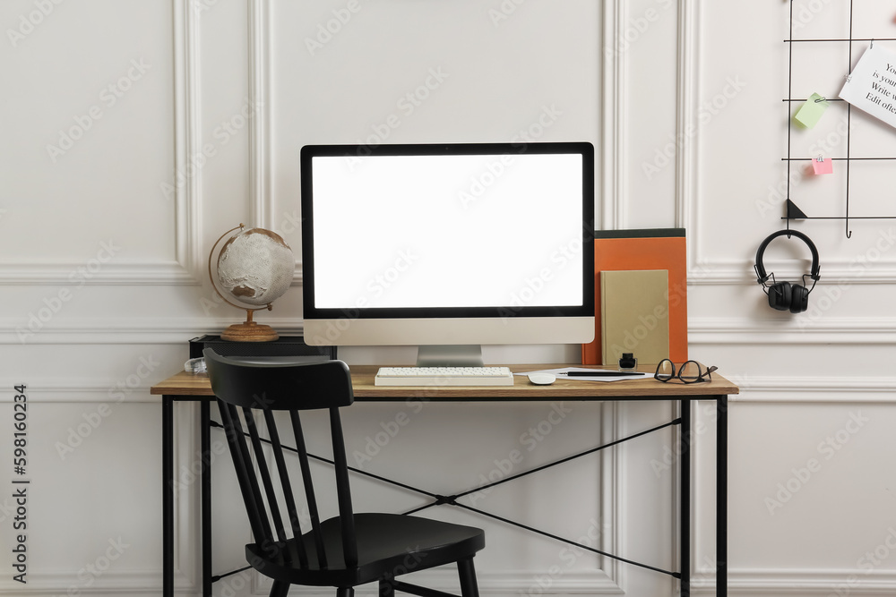 Stylish workspace with computer and stationery on wooden desk near white wall indoors Stylish workspace with computer and stationery on wooden desk near white wall indoors