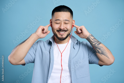 Handsome happy asian man with stylish tattoo, wearing headphones listening music